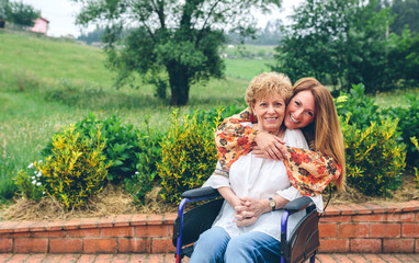 Daughter embracing her senior mother in wheelchair - Powered by Adobe