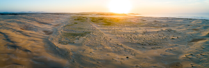 Aerial panorama of sunrise over sand dunes near ocean