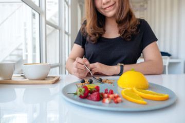 A beautiful asian woman enjoyed eating orange cake with mixed fruit by spoon in cafe