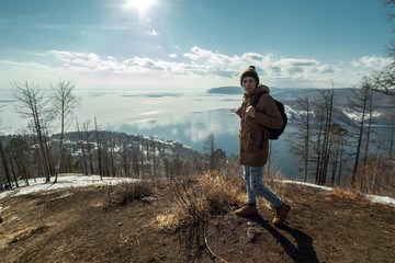 Traveler stands on a mountain and looks at the beautiful view of lake Baikal. Winter landscape.