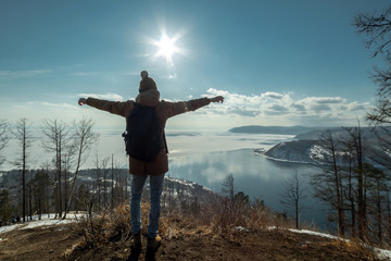 Man tourist traveler stands on a mountain and looks at the beautiful view of lake Baikal. Winter landscape.