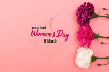 International Women's Day with flowers and heart shape necklace on pink background
