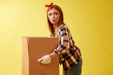 People moving new place and repair concept - Young woman holding cardboard box. Yellow background.