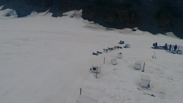 Aerial of huskies and with a dogsled and the camp on top of a glacier.