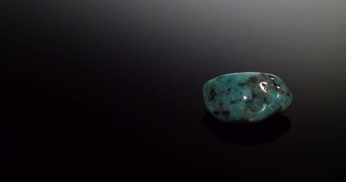 A blue turquoise mineral stone isolated on a black reflective background.