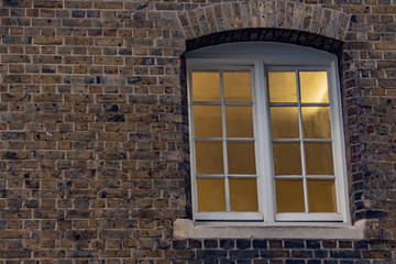 Fototapeta na wymiar Light shining through the sash window at night. Brick wall facade.
