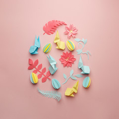 Easter egg shape made of various Easter origami paper craft decorative elements on pink background. Minimal spring concept. Flat lay.