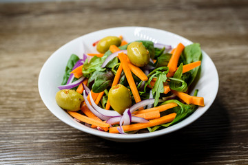 Freshly made vegetable salad with carrot, olives, spinach and onion in a bowl on wooden background.