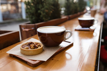 Fototapeta premium two cups of coffee cappuccino with baked dessert on wooden table cappucino on wooden table and girl defocussed on the background cappucino with baked dessert on wooden table