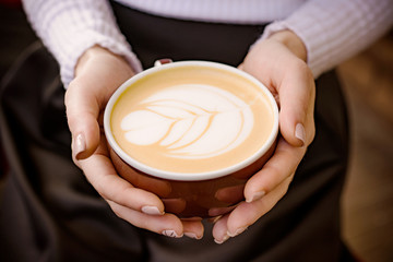 cup of coffee cappuccino in girl's hands on a dark background, macro