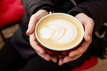cup of coffee cappuccino in girl's hands on a dark background, macro