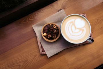 cup of coffee cappuccino with baked  nuts and caramel dessert on wooden table