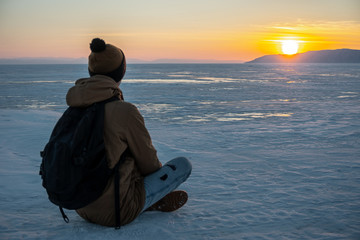Traveler with a backpack watching the sunset on the snowy ice of lake Baikal. Concept of freedom and travel