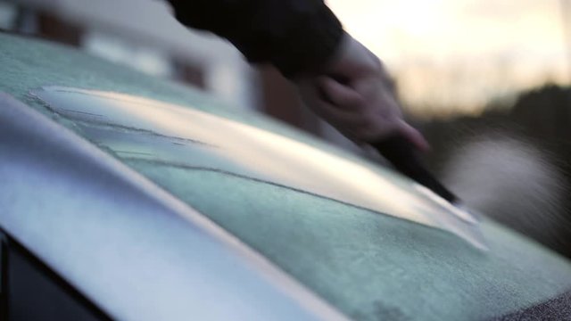 Using an ice scrapper to remove ice from a car windscreen on a cold winter morning.