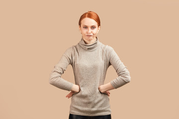 Skinny young woman with sad and disappointed expression, keeping hands on both sides, isolated over beige background.