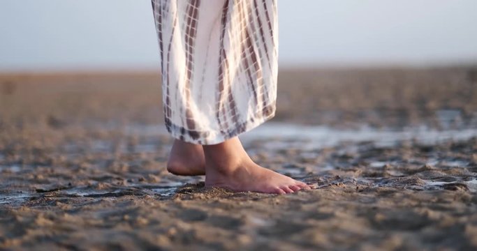 Low angle and closeup of a girl's feet standing on a wet sand at a beach near the sea