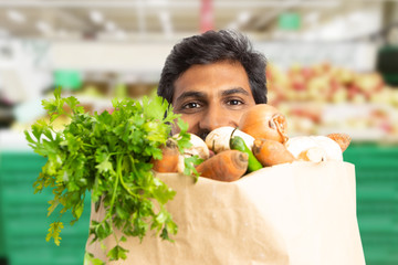 Close-up of supermarket employee hiding behind grocery bag.