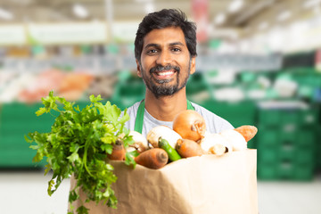 Grocery store employee holding bag of vegetables.