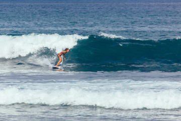 Young asian woman in green bikini surfing turquoise wave in Bali 