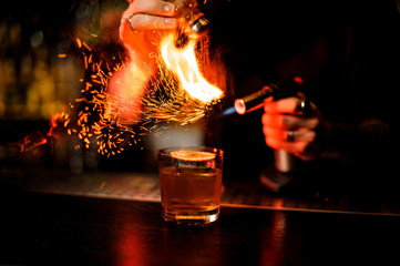 Bartender adding to a cocktail brown spice and flame it
