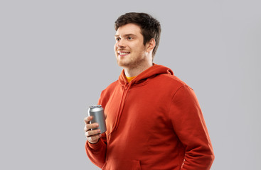 drinks and people concept - happy young man in red hoodie drinking soda from tin can over grey background