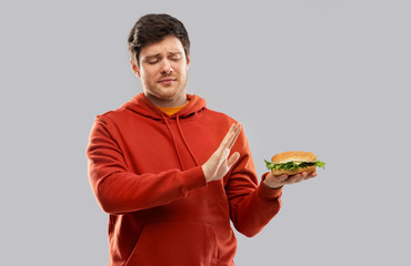 fast food, unhealthy eating and people concept - young man in red hoodie refusing from hamburger...