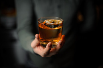 Bartender serving a delicious brown cocktail with a dried orange on the blurred background