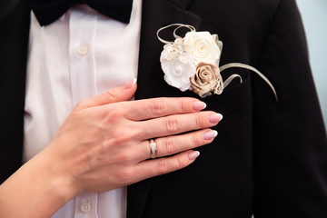 Wedding boutonniere on suit of groom and the hand of bride 