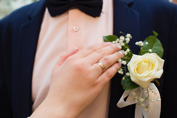 Wedding boutonniere on suit of groom and the hand of bride 