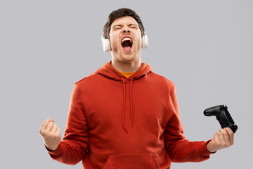 technology, gaming and people concept - happy young man or gamer in headphones with gamepad winning...