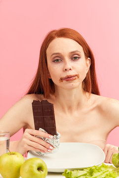 Enjoying taste. Red-haired woman tired of diet restrictions enjoying taste of dark chocolate, prefer it to healthy vegetables. Human face expression emotion. Nutrition concept. Feeling of guilt.