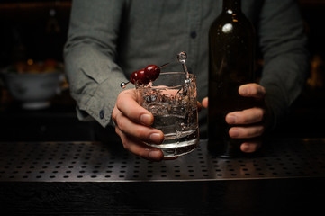 Bartender serving a cocktail glass decorated with a berries on a skewer