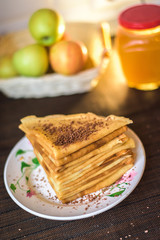 pancakes on a plate with honey and chocolate. stacked pyramid. on the background of a jar of honey and apples. carnival