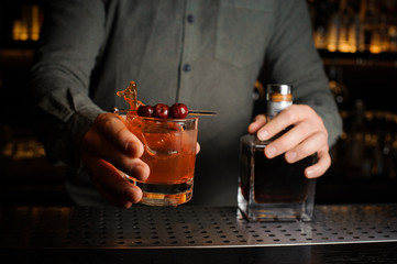 Professional bartender serving a cocktail glass decorated with a berries on the caretaker
