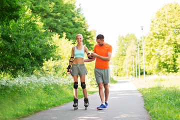 fitness, sport and healthy lifestyle concept - happy couple with roller skates riding outdoors in...