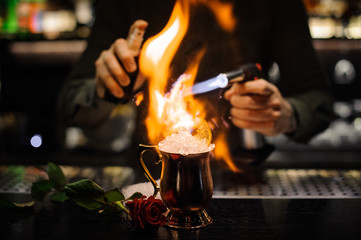 Bartender spraying on the cocktail in the golden cup and flaming it