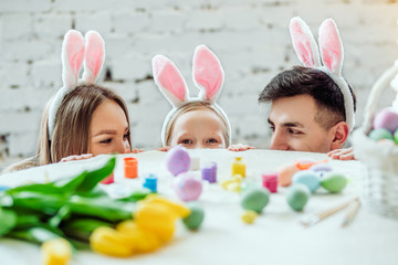 Obraz na płótnie Canvas Let's play together.Lovely family preparing for Easter together. Happy mom,daughter and father are hiding around the table and looking at each other.