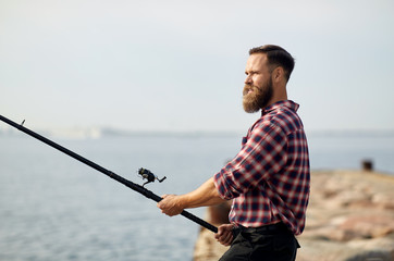 leisure and people concept - bearded fisherman with fishing rod on pier at sea