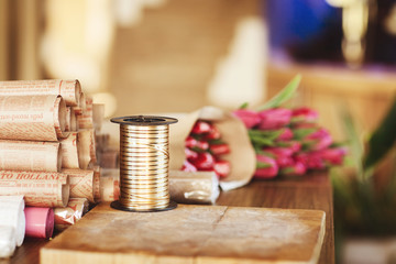 On a wooden table lies craft paper wrapping tape and pink tulips. Side view