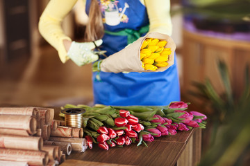 Naklejka na ściany i meble Girl packs colorful bouquets of tulips in craft paper