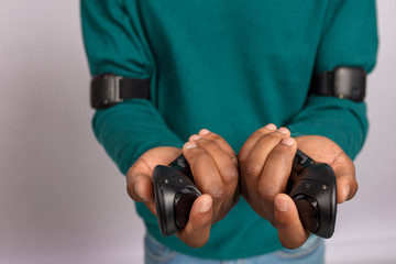 Close up shot of hands in green sweater holding controllers from virtual reality headset. Grey background. VR technology gadget.
