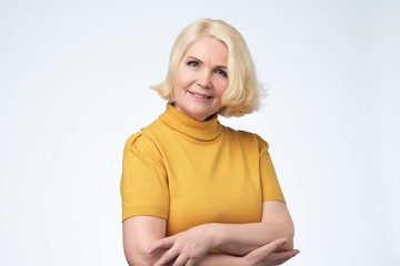 Beautiful older woman smiling and standing by wall