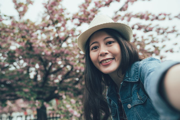 Woman taking self photo in spring season with pink cherry tree. young girl traveler wear hat...