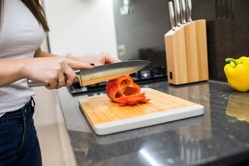 Young woman cooking in the kitchen healthy food, vegetable Salad. Holding a knife and cutting vegetables on a cutting board. Healthy lifestyle cooking at home.