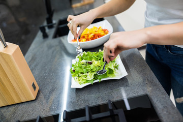 Beautiful young girl in a white shirt prepares healthy food with greens. Woman mixed salad in kitchen.