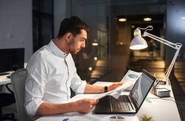 business, deadline and people concept - businessman with laptop computer and papers working at...