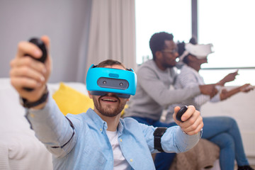 Happy man trying on 3D virtual reality goggles. while african room mate teaching his girl to master gadget. Having fun trying new technologies. Virtual adventure.
