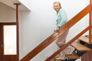 Elderly woman at home using a cane to get down the stairs