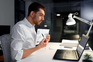 business, technology and people concept - businessman with charts having video chat on laptop computer at night office