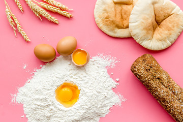 Ingredients for homemade bread. Bread near wheat ears, flour and eggs on pink background top view